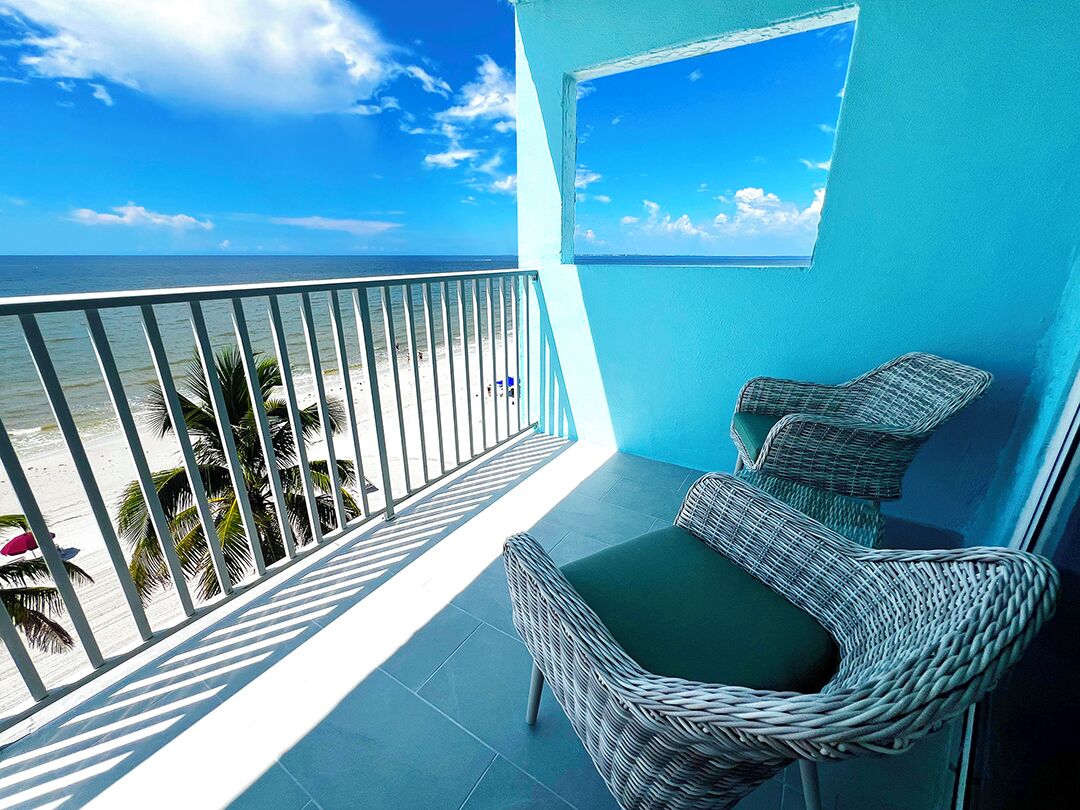 A balcony with wicker chairs and a view of the beach.