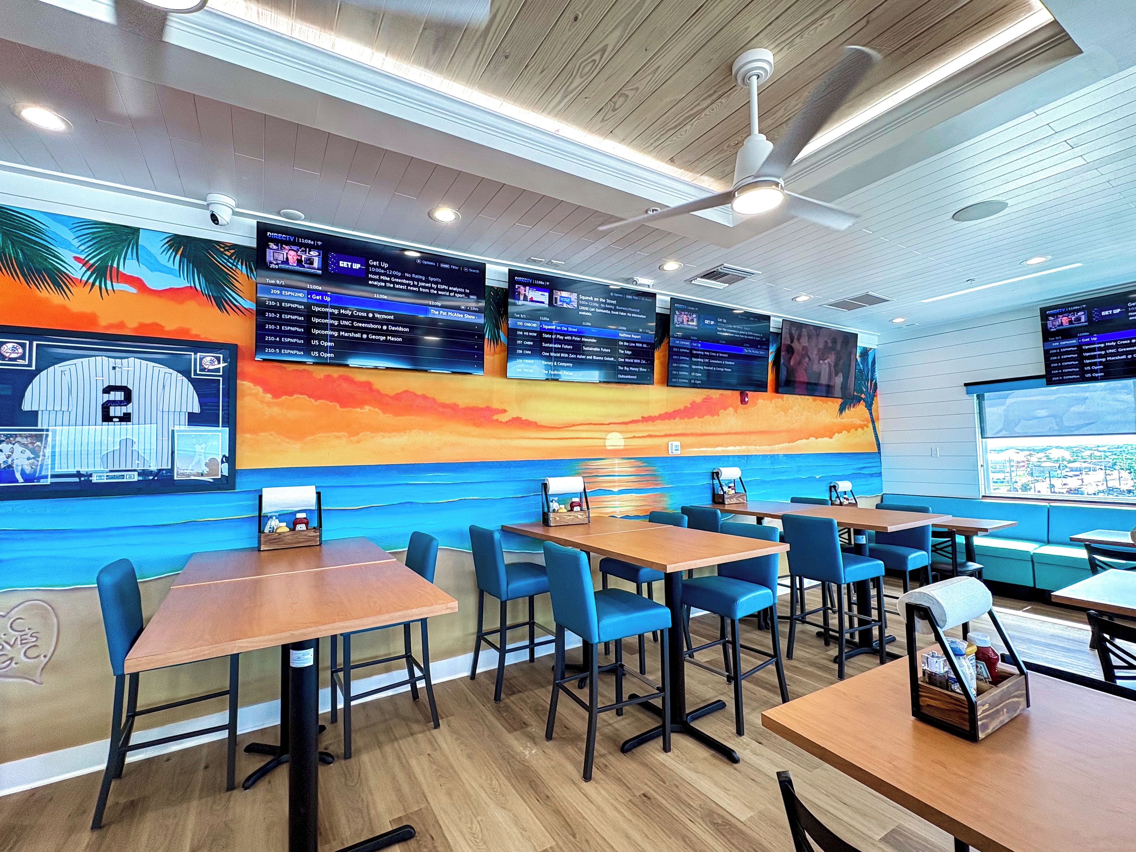 A restaurant interior with multiple tables, chairs, and a large mural on the wall.