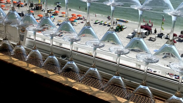 Vista a la playa con hileras de copas de vino vacías alineadas en un balcón.