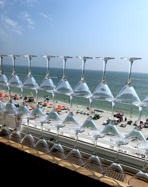 A beach view with rows of empty wine glasses lined up on a balcony.