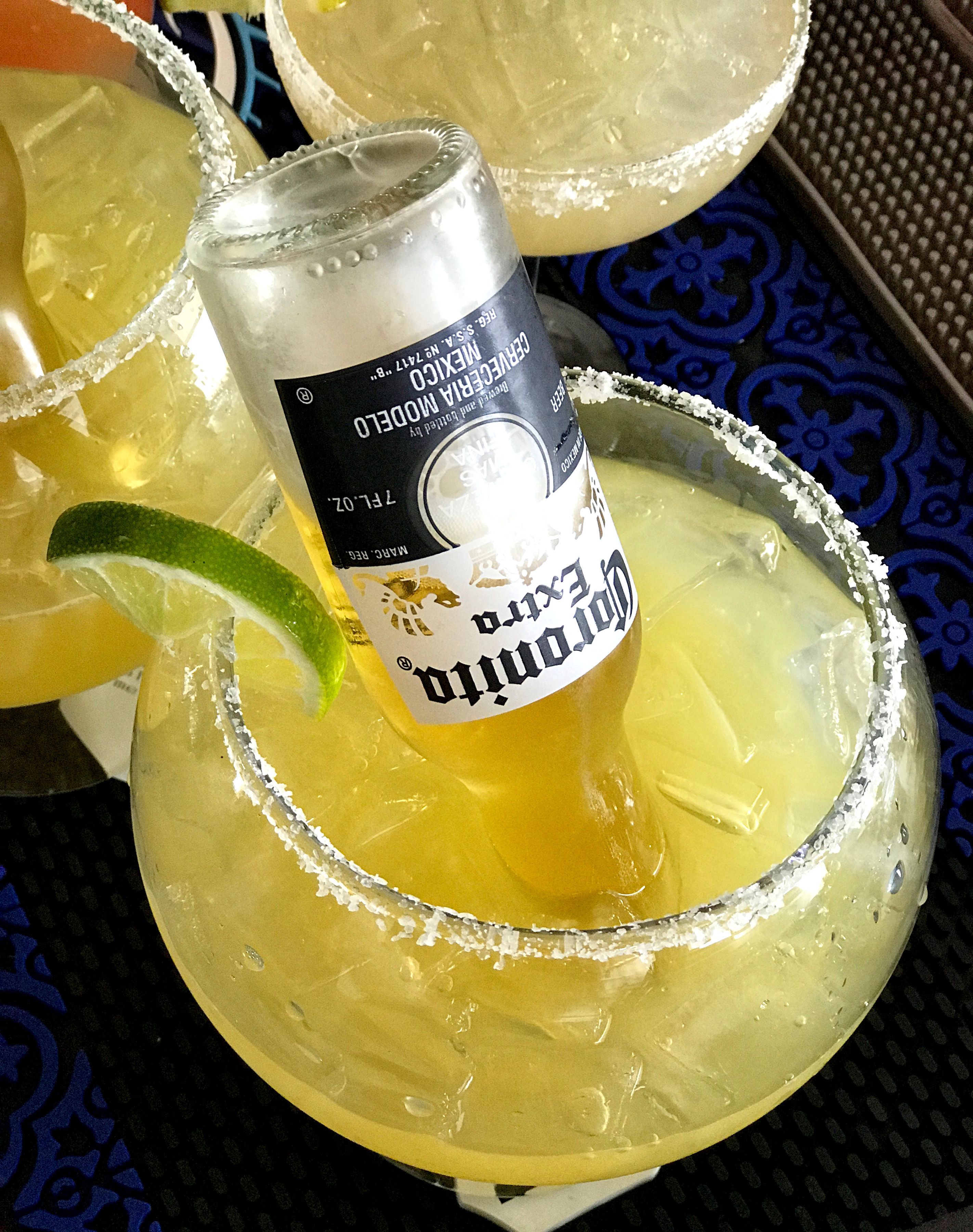 Ein Margarita-Glas mit einer Limettenscheibe und einer Corona-Bierdose am Rand.