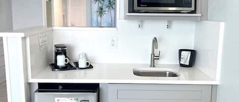A compact kitchen with a built-in microwave, a stainless steel refrigerator, and a sink.