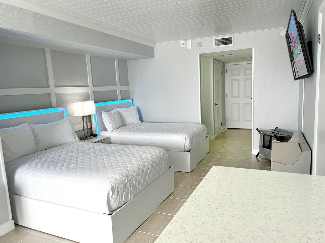 A modern hotel room with two beds, a desk, a TV, and a bathroom visible through an open door.