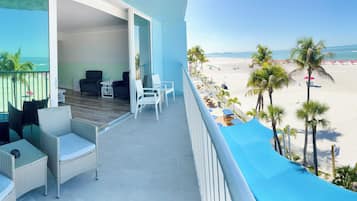 Ein Balkon mit Korbmöbeln, Blick auf einen Strand und einen klaren Himmel.