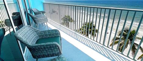 A balcony with wicker furniture overlooking a beach.