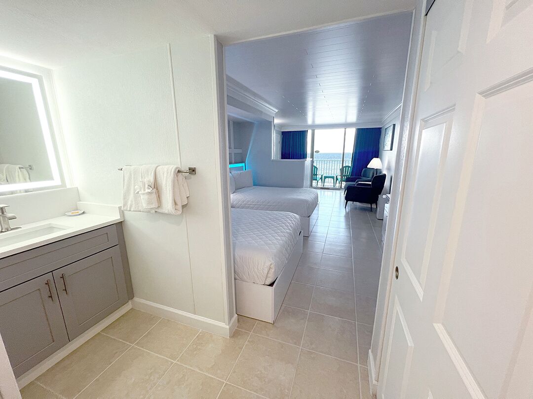 A modern hotel room with a bathroom, a balcony with a view, and a seating area.