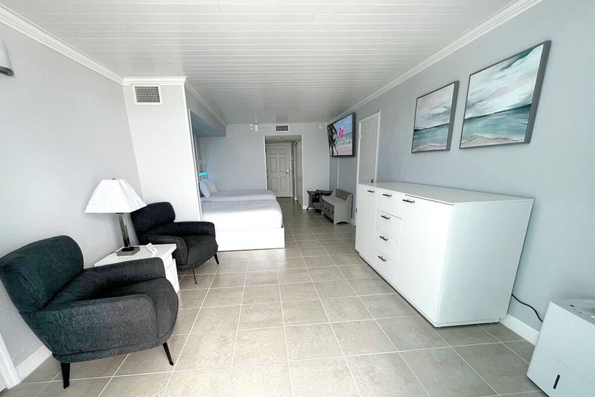 A hotel room with a bed, a desk, a chair, a TV, and artwork on the wall.