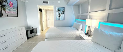 A hotel room with two beds, a desk, a nightstand, and a wall-mounted TV.