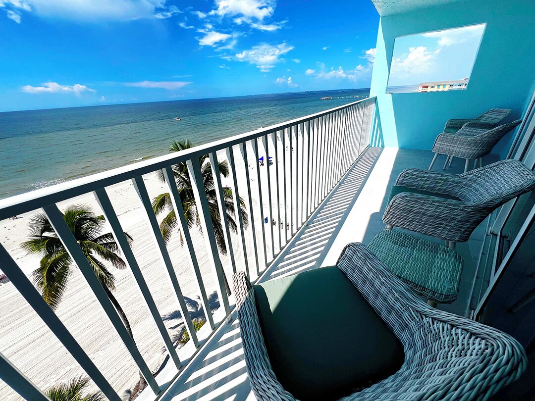 A balcony with wicker chairs and a view of the beach and ocean.