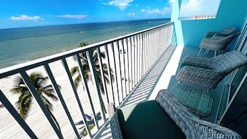 A balcony with wicker chairs and a view of the beach and ocean.