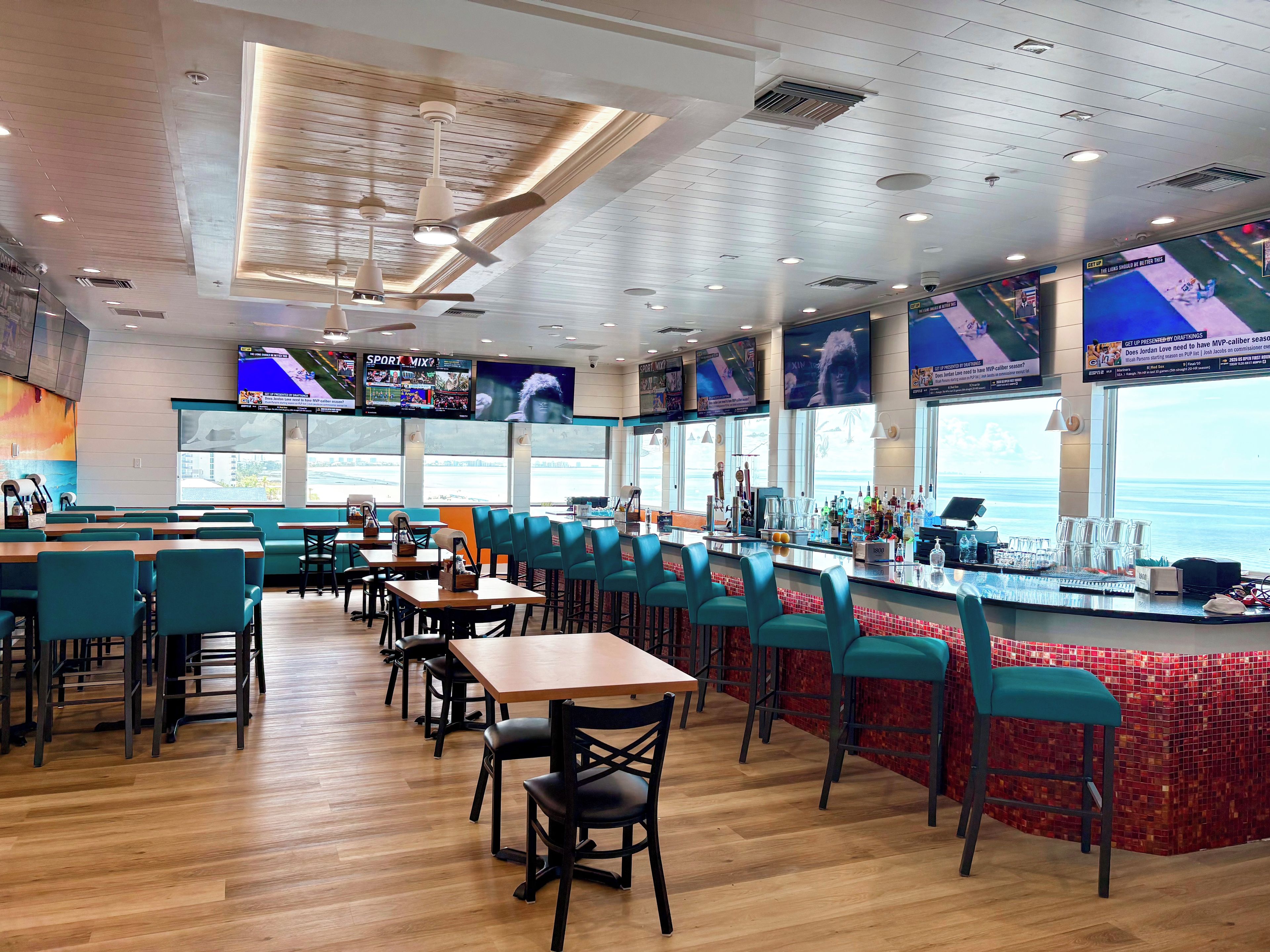 A restaurant with a bar area, seating, and large windows.