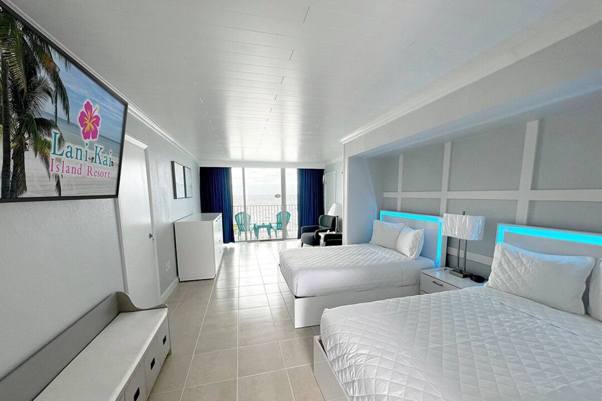 A hotel room with two beds, a desk, and a balcony with a view of the ocean.
