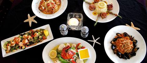 A table set with various seafood dishes, including pasta, shrimp, and mussels, arranged on a black tablecloth.