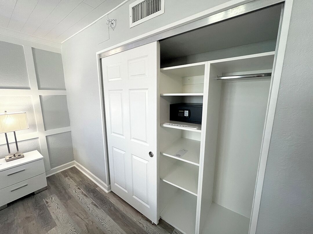 A walk-in closet with white shelving, a door, and a small table with a lamp.