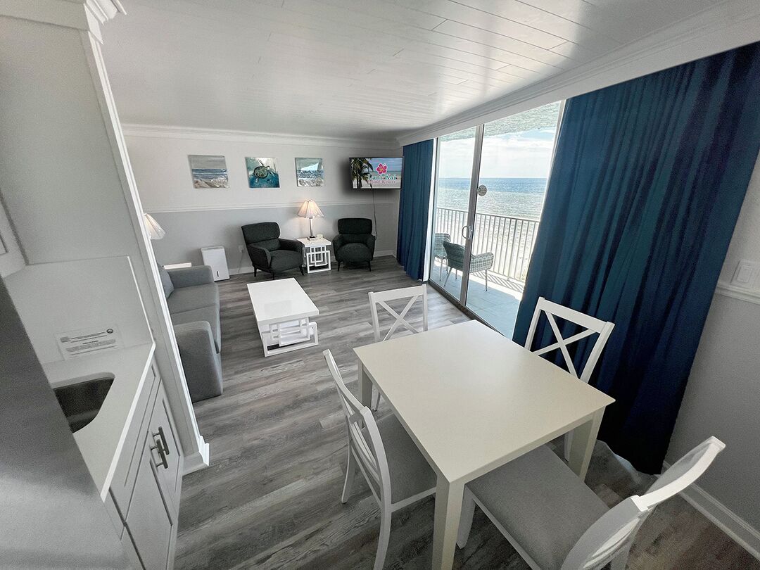 A compact living space with a dining area, a sofa, a TV, and a balcony with a view of the sea.