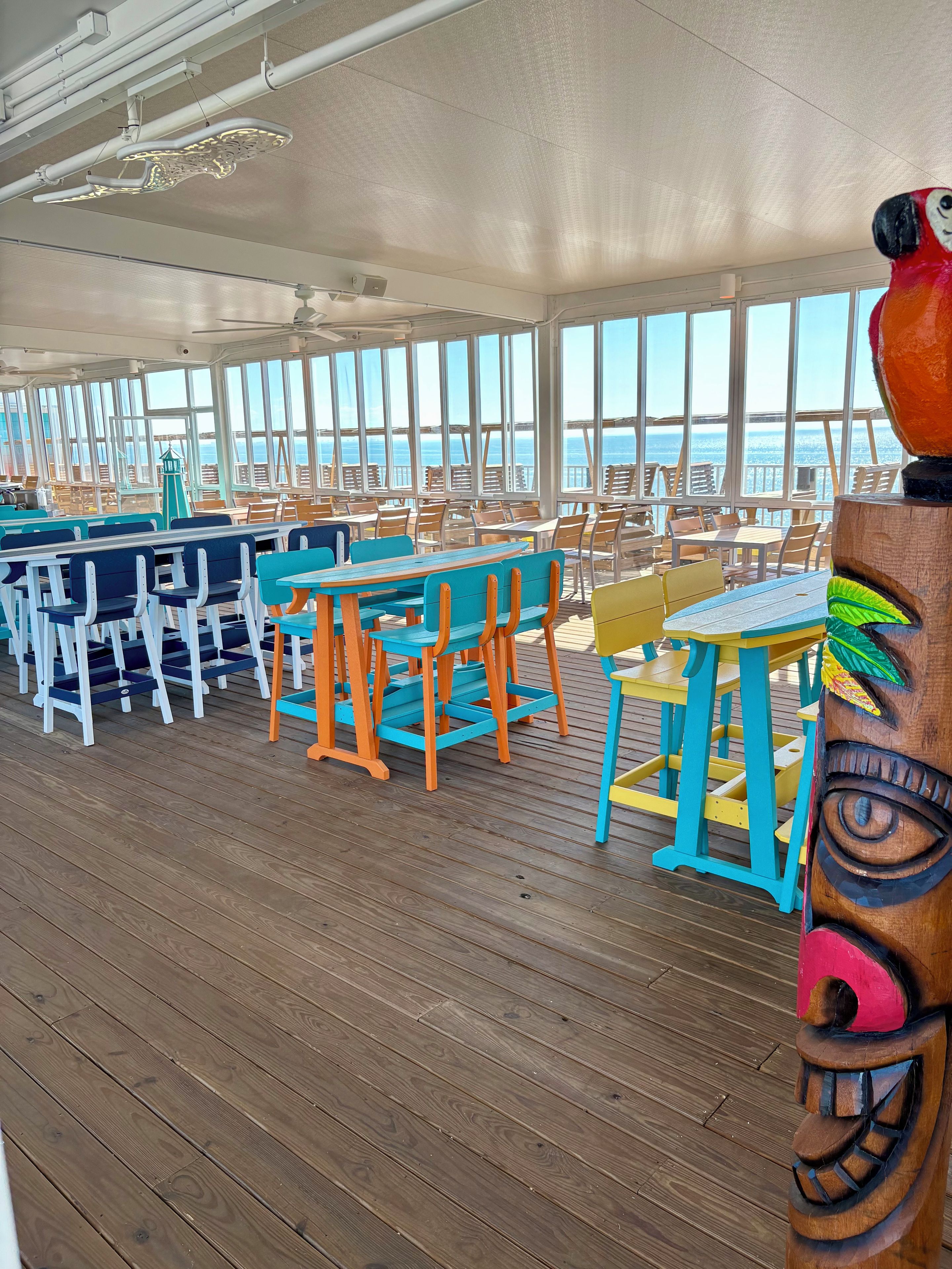 A deck with tables and chairs, large windows, and a view of the ocean.