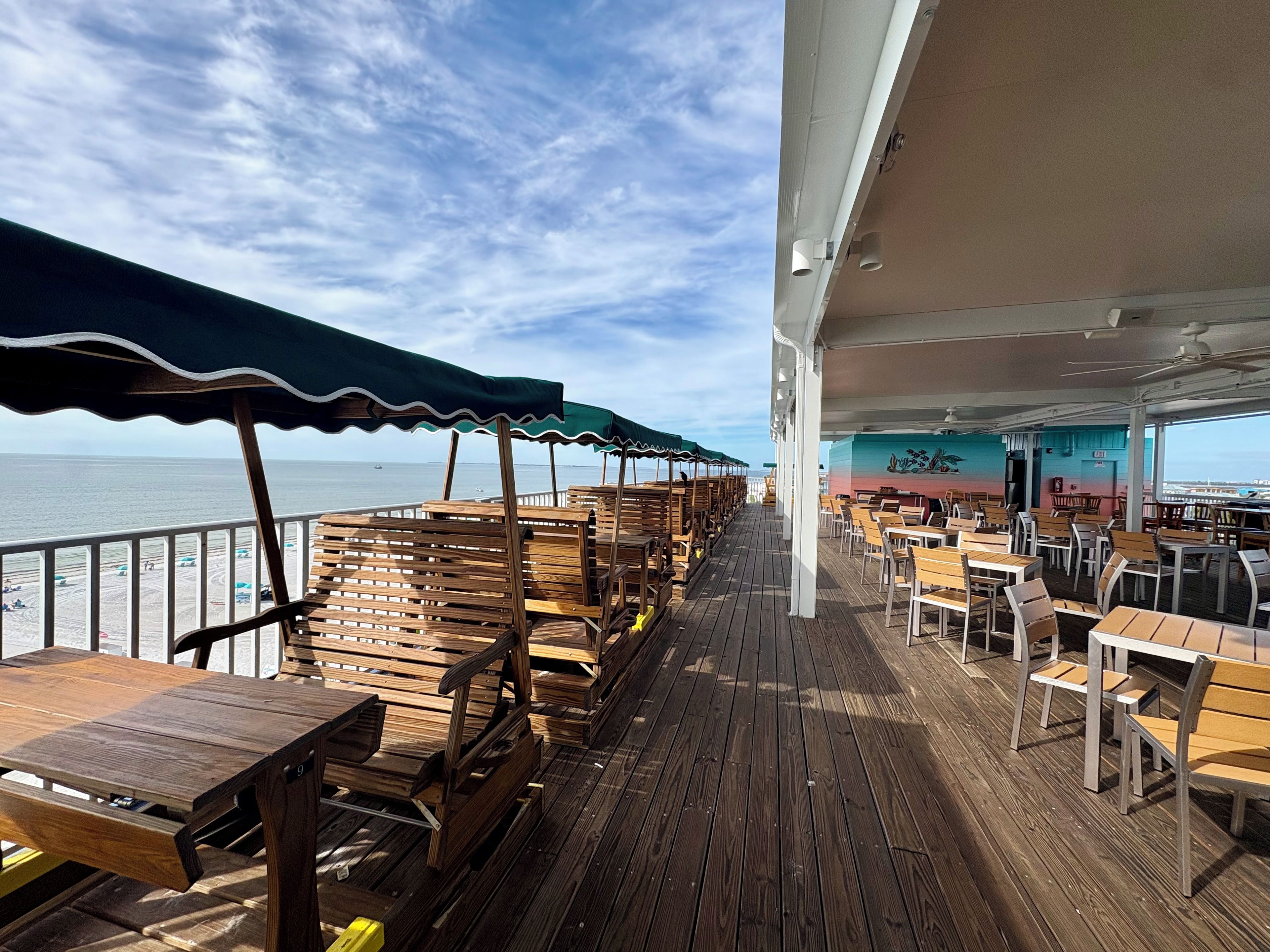 Une terrasse avec des bancs et des tables en bois, une rambarde et une vue sur la mer.