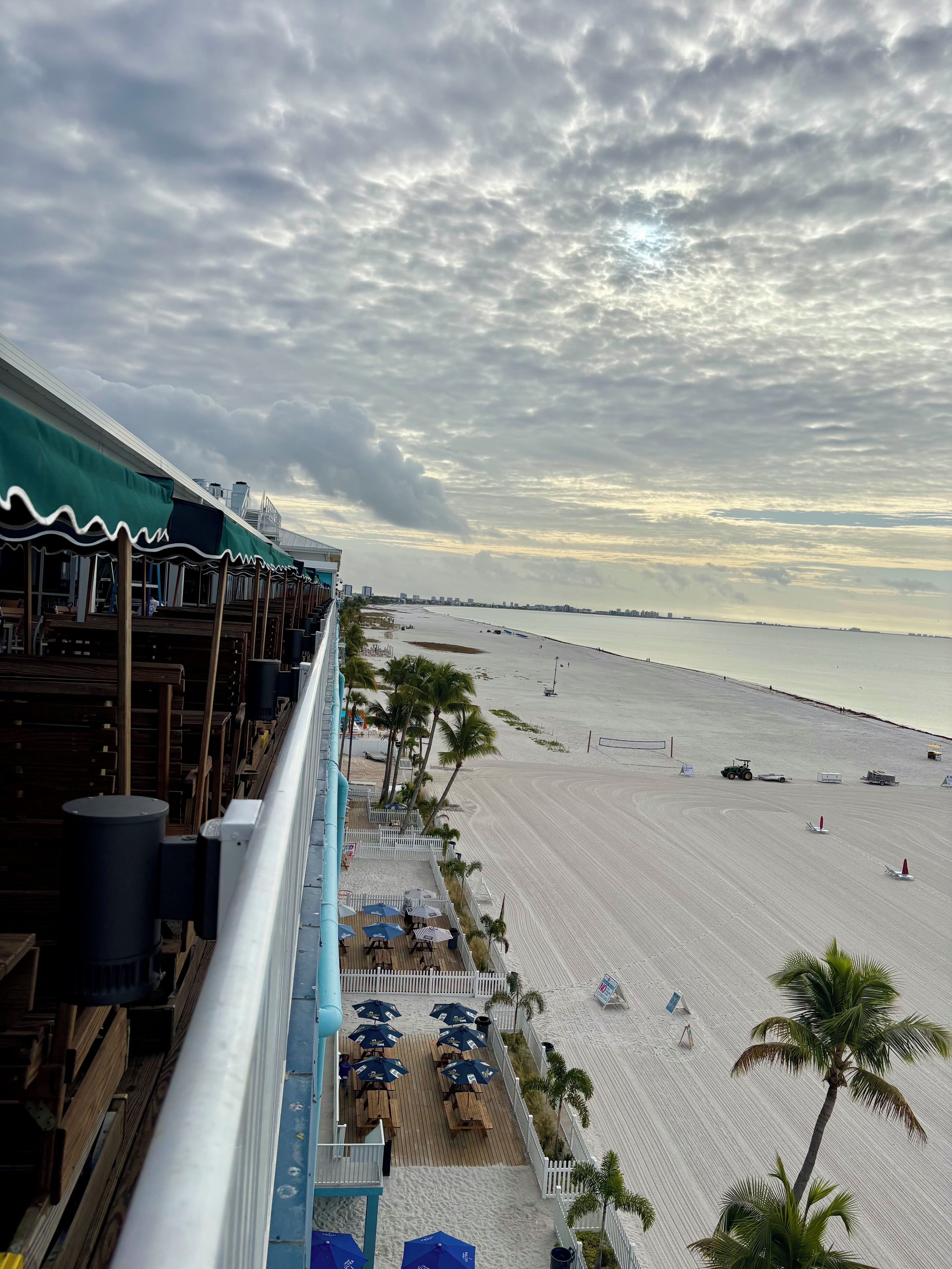 A beachside view with a wooden deck and umbrellas, overlooking a sandy beach and the ocean.