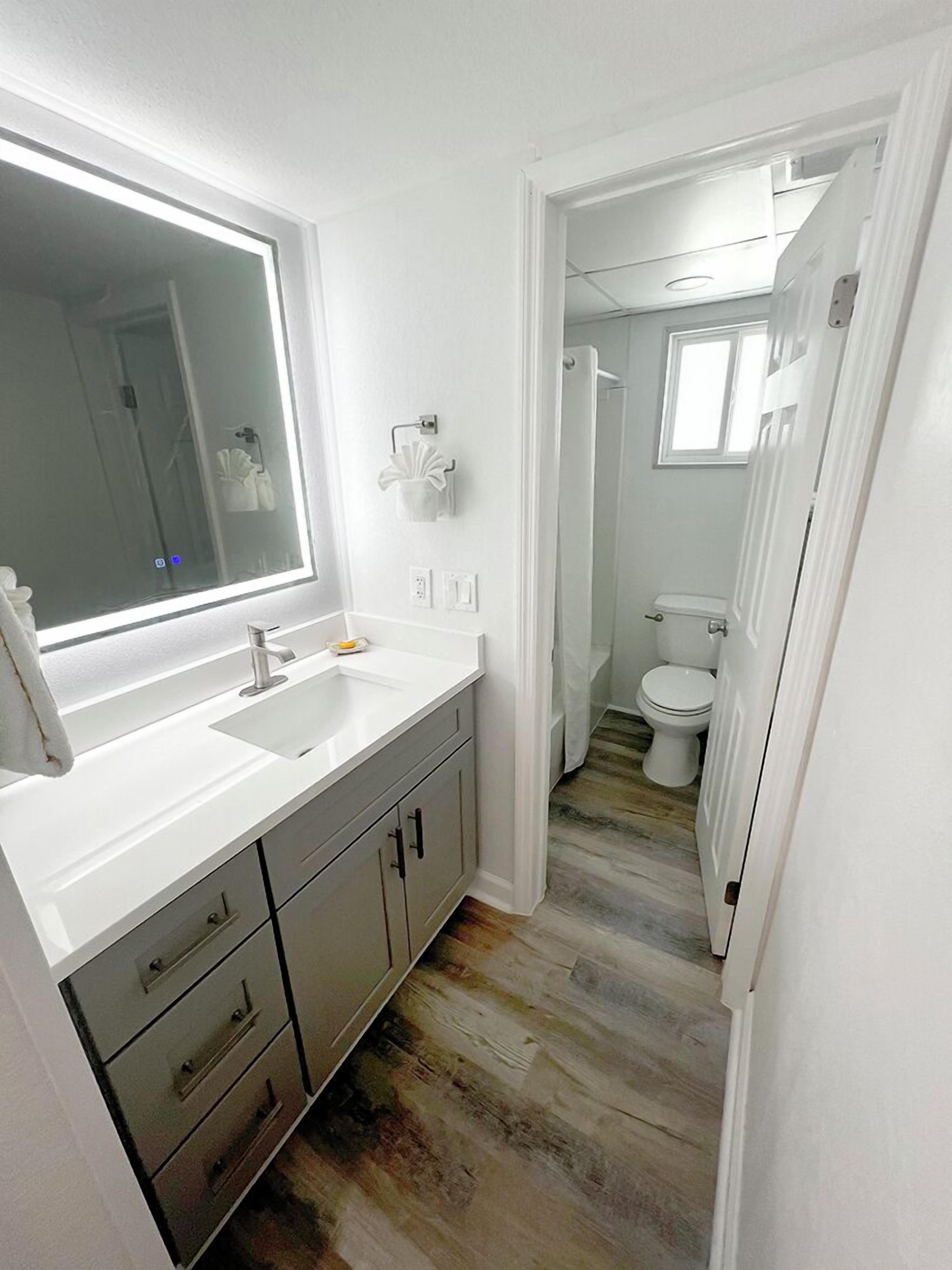 Un baño moderno con un espejo grande, encimeras blancas y una ducha a ras de suelo.