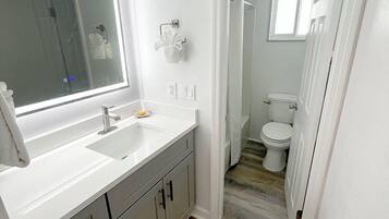 Une salle de bain moderne avec un grand miroir, des plans de travail blancs et une douche à l’italienne.