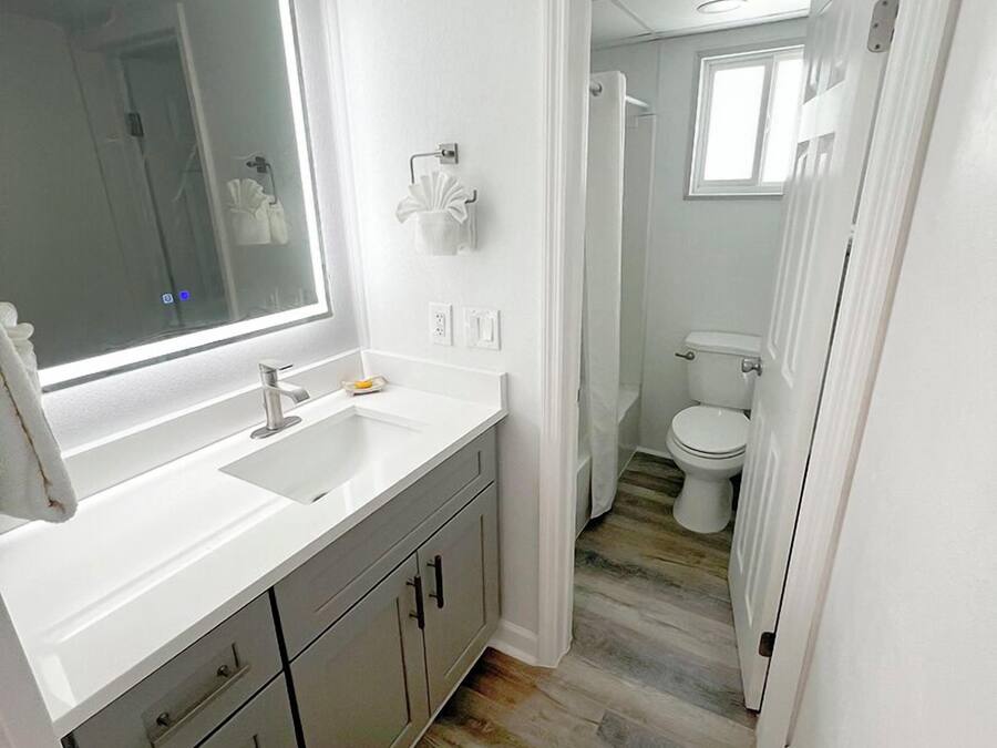 Une salle de bain moderne avec un grand miroir, des plans de travail blancs et une douche à l’italienne.