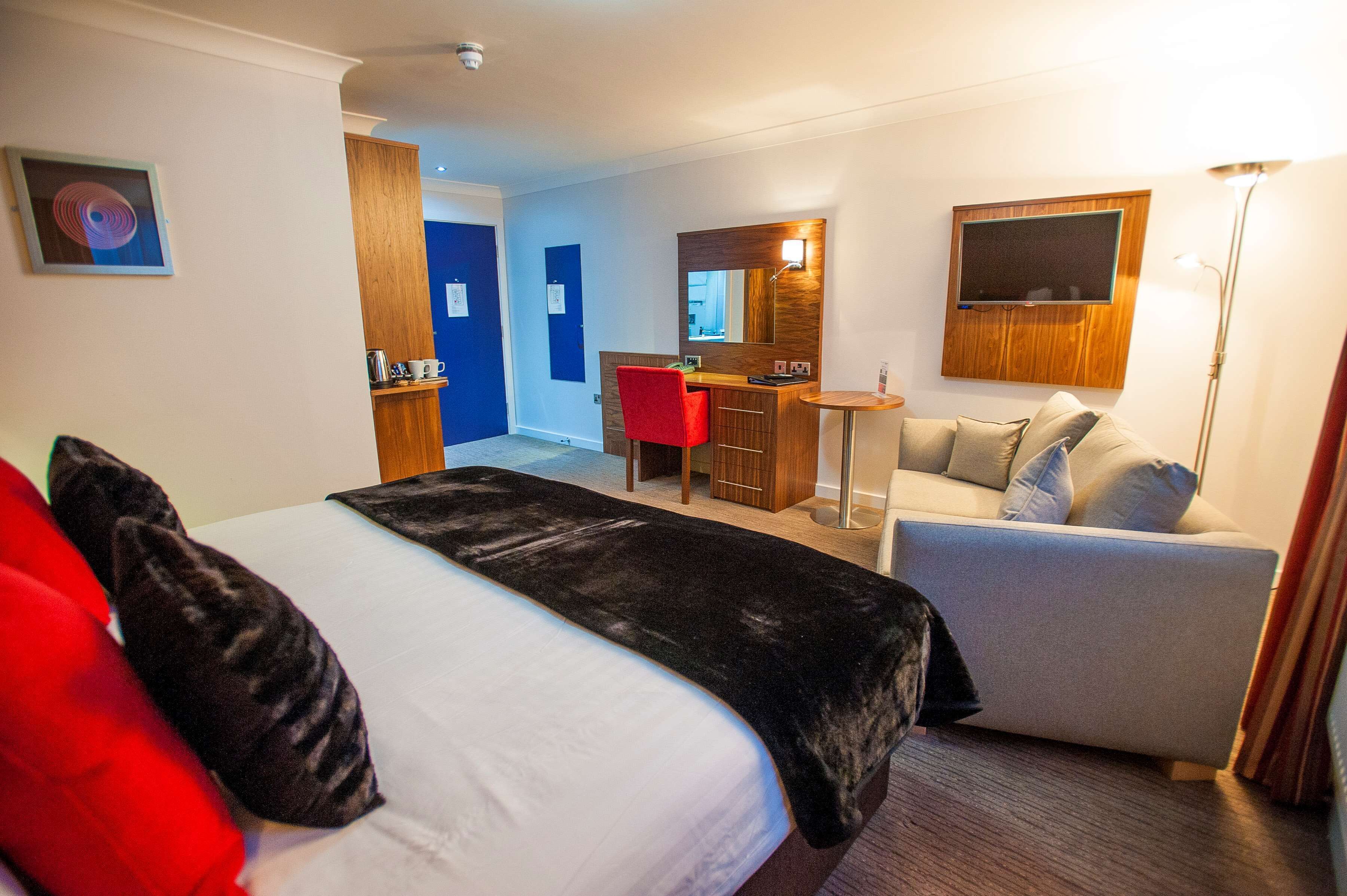 Una habitación de hotel con cama, escritorio, sofá y televisión.