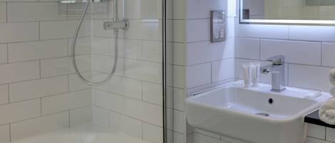 Een moderne badkamer met een douchecabine van glas, een wit wastafeltje met een spiegel erboven en een handdoekhouder.