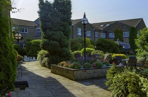 A courtyard with stone paving, outdoor seating, and a building with multiple windows and a sloped roof. - Lancashire Manor Hotel, BW Signature Collection (Skelmersdale)
