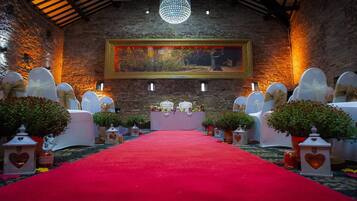 An aisle with white chairs and a red carpet, leading to a stage with a framed painting.