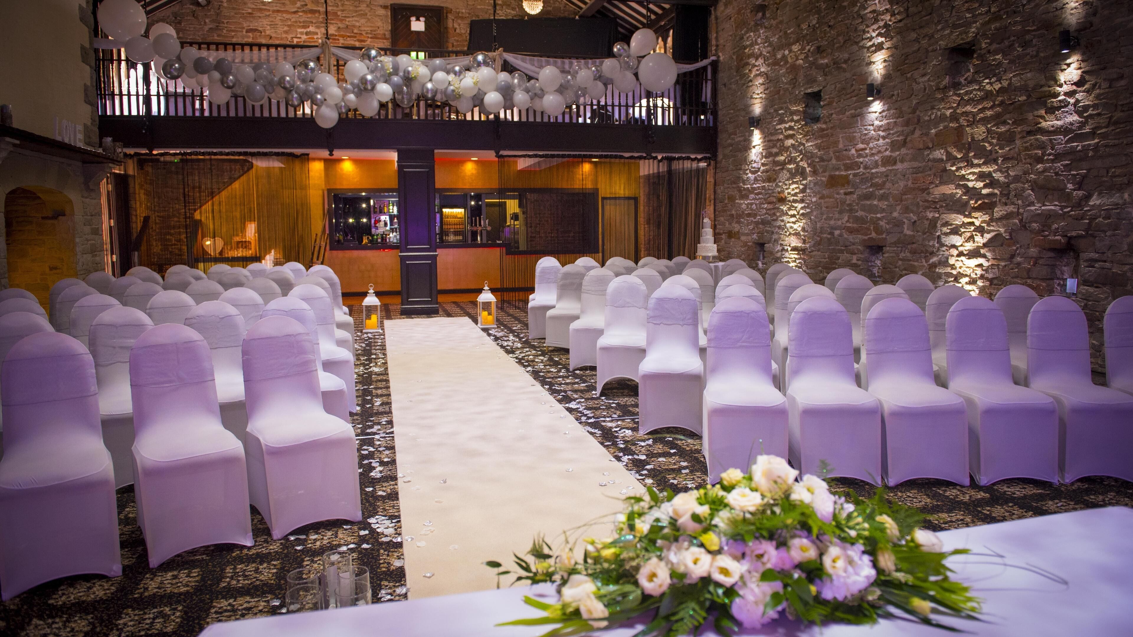 An indoor venue with rows of white chairs, a central aisle, and a balcony with balloons.