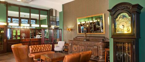 A lobby with a bar area, leather furniture, a large clock, and a green tiled wall.