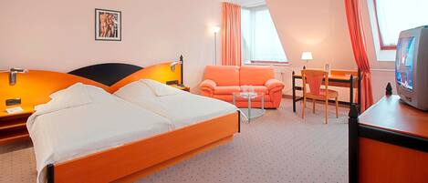 Habitación de hotel con cama doble, sofá, escritorio, silla, televisor y ventana con cortinas.