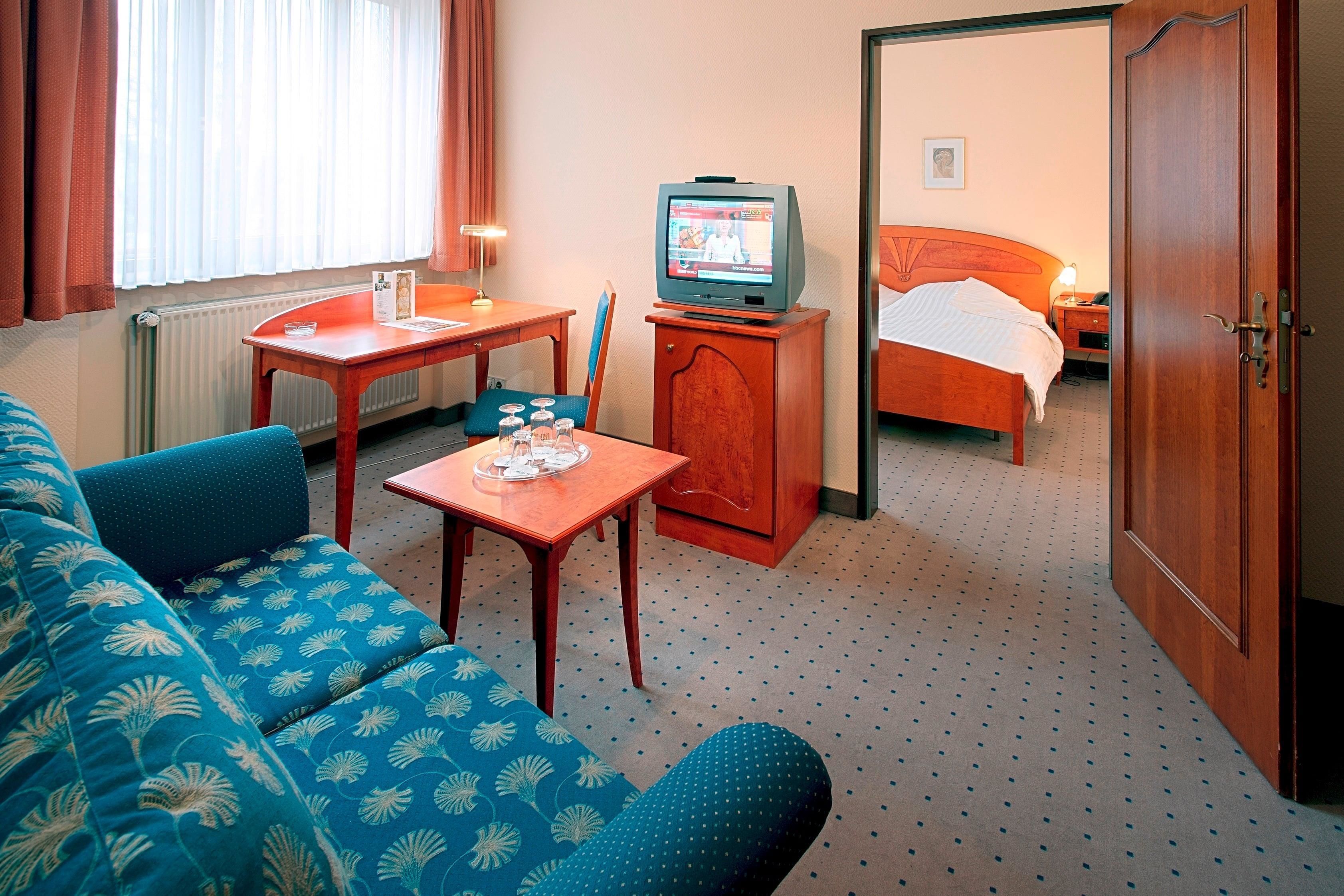 Habitación de hotel con sofá, una mesita con bandeja, televisor, cama y puerta.