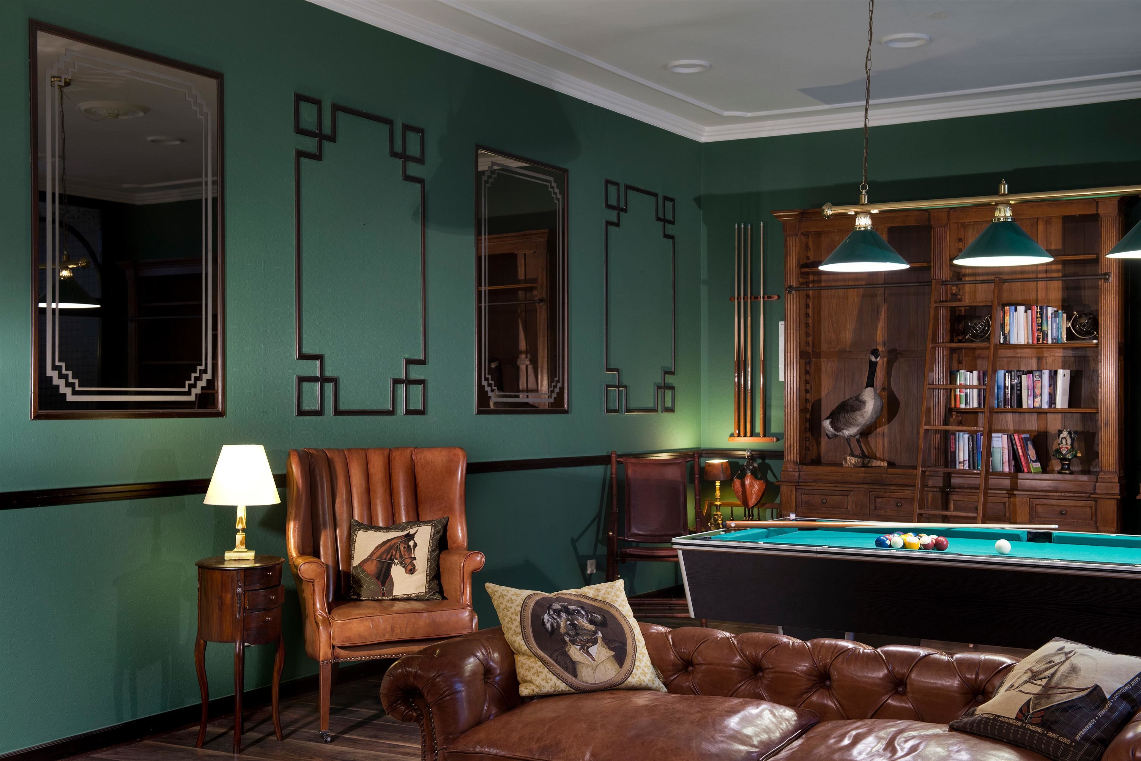 Una habitación con mesa de billar, sillones de cuero, una estantería y un espejo grande.