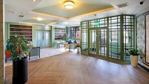 Een ruime lobby met houten vloeren, een zithoek met een tafel en stoelen, en een grote boekenkast.