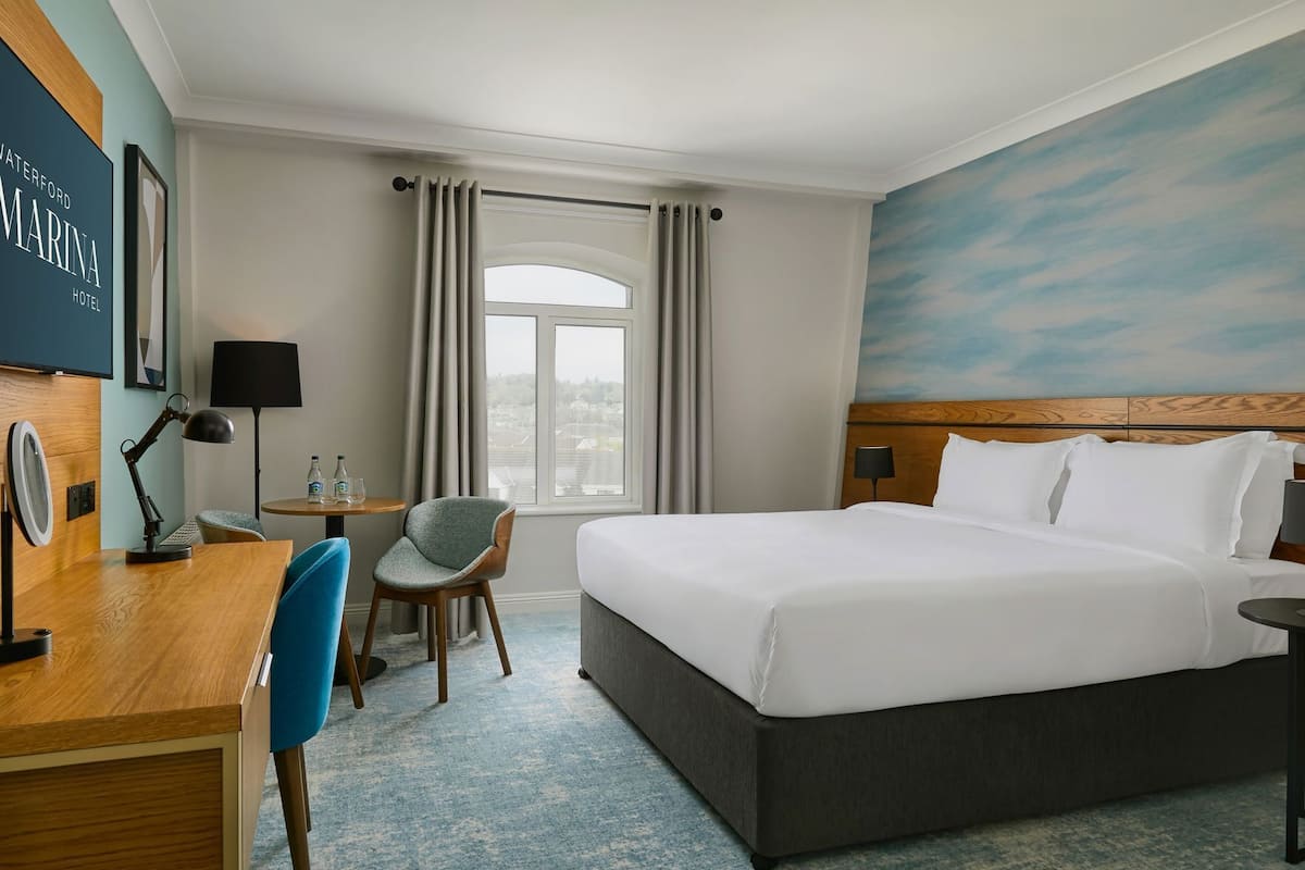 Une chambre d’hôtel équipée d’un lit, d’un bureau, d’une chaise, d’une lampe et offrant une vue sur l’extérieur.