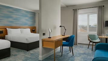 A hotel room with a bed, a desk with a chair, a small table with a chair, and a large window with curtains.