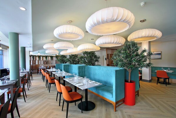 A restaurant with teal booths, orange chairs, and white pendant lights.