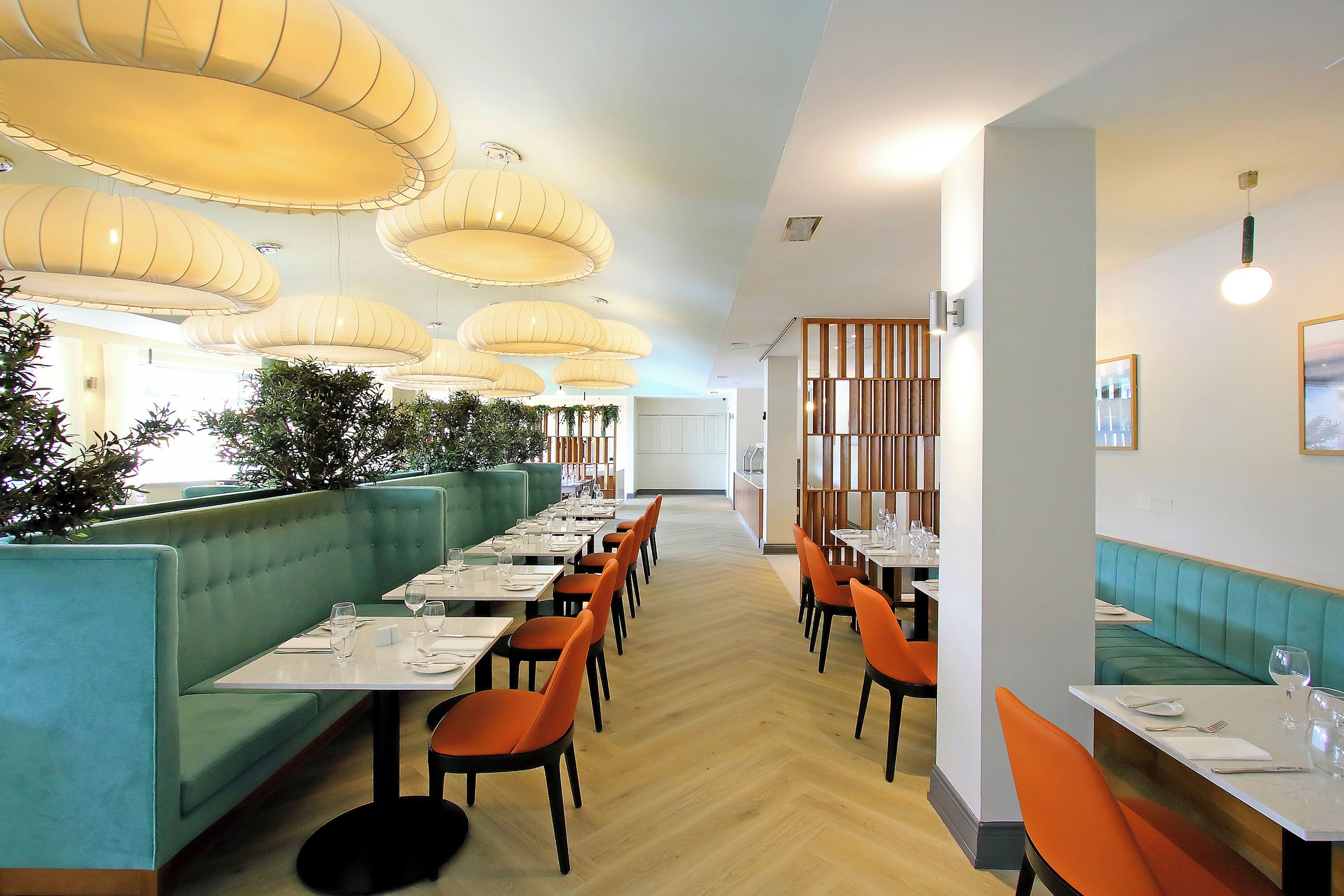 Un restaurante con asientos tipo banca color turquesa, sillas naranjas y piso de madera.