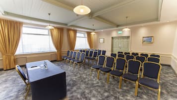 Un salón de conferencias con filas de sillas, una mesa y suelo alfombrado.