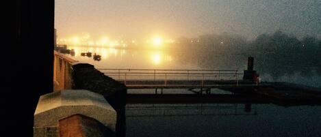 A waterfront view with a bridge, a railing, and distant lights reflecting on the water.