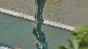 A bronze sculpture of a human figure in a dynamic pose, situated by a body of water.