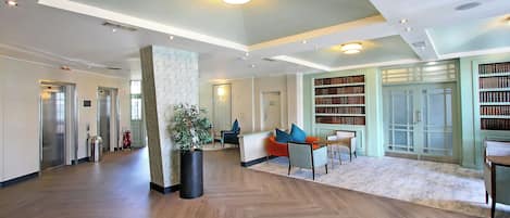 A spacious lobby with a herringbone wood floor, a reception desk, seating area, and a large bookshelf.