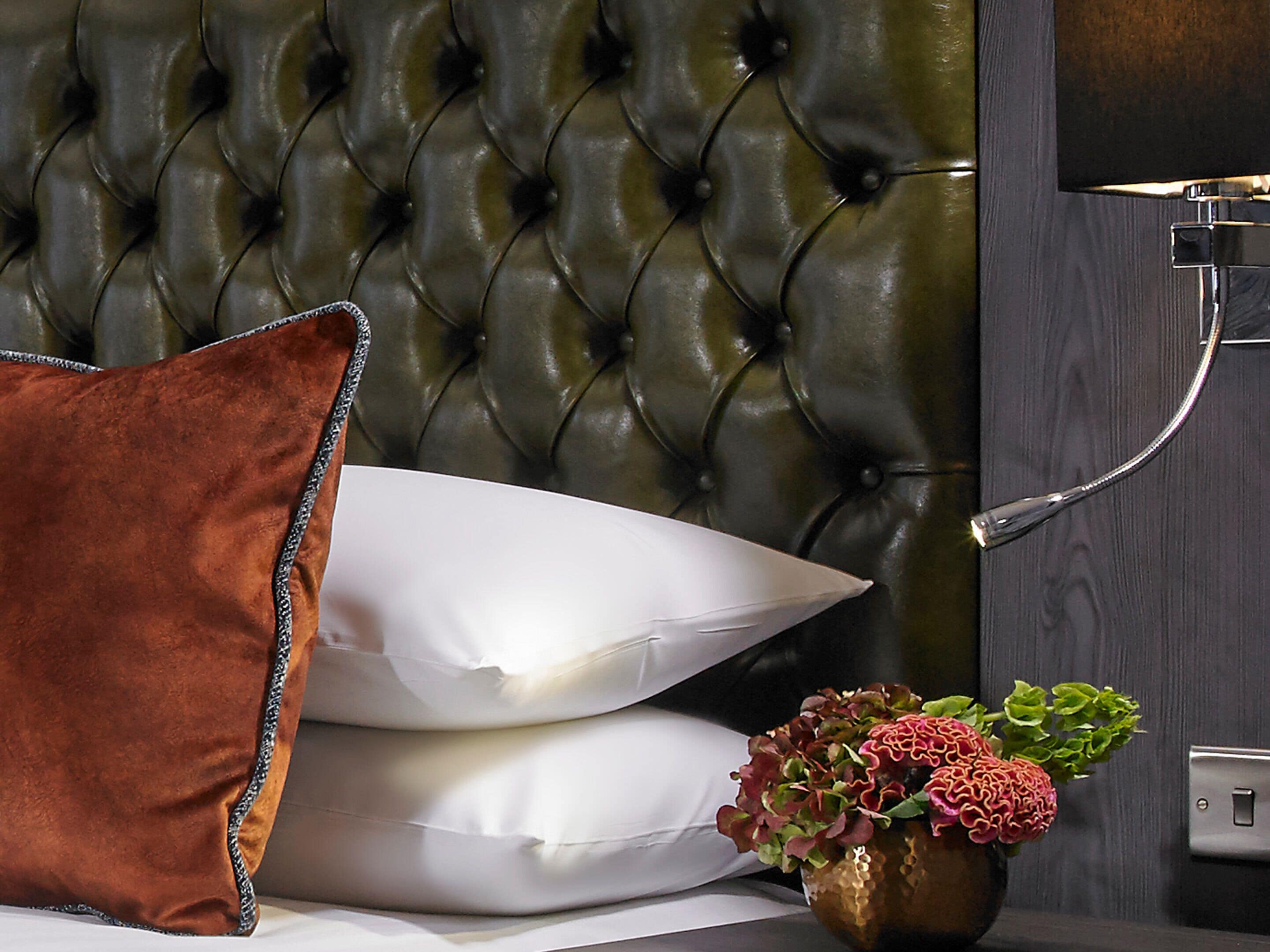 A tufted headboard, a white pillow, a brown pillow, and a vase with flowers.