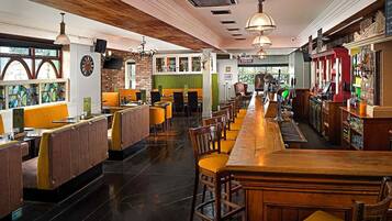 Un bar con taburetes de madera y una barra larga. Se ven mesas y sillas al fondo.