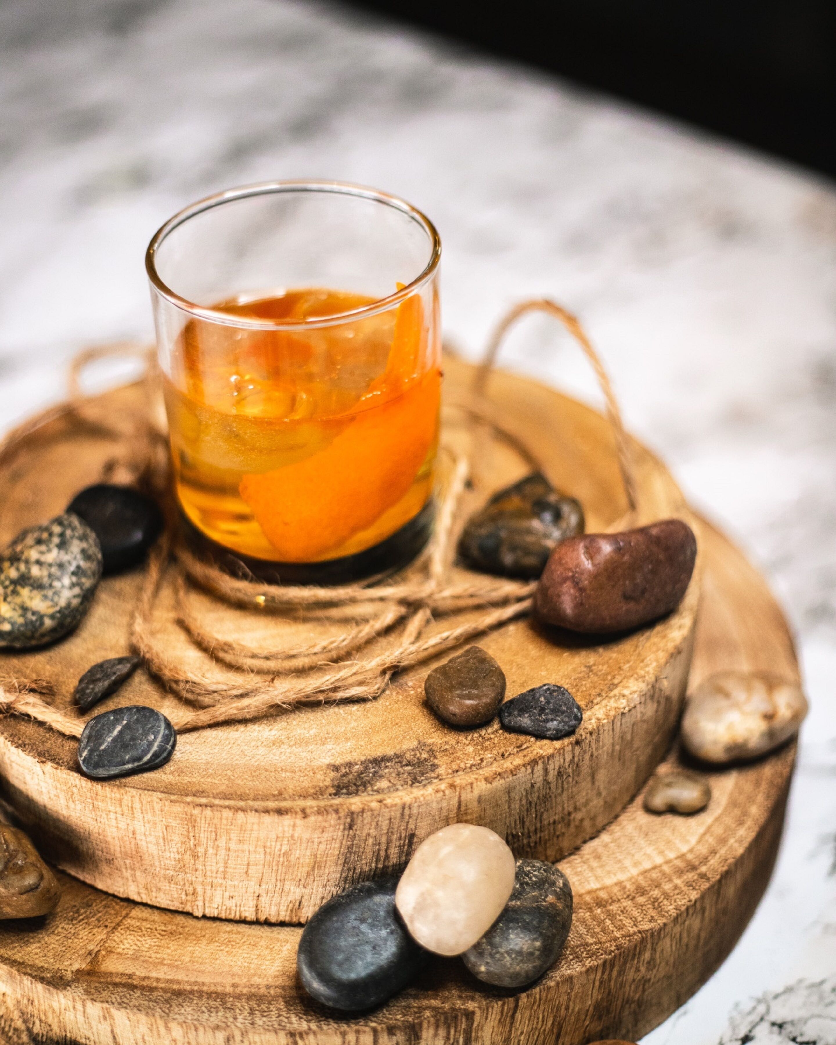 Un vaso de líquido ámbar sobre un posavasos de madera, rodeado de piedras lisas.