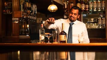 Un cantinero detrás de la barra, con una variedad de botellas de licor y vasos.