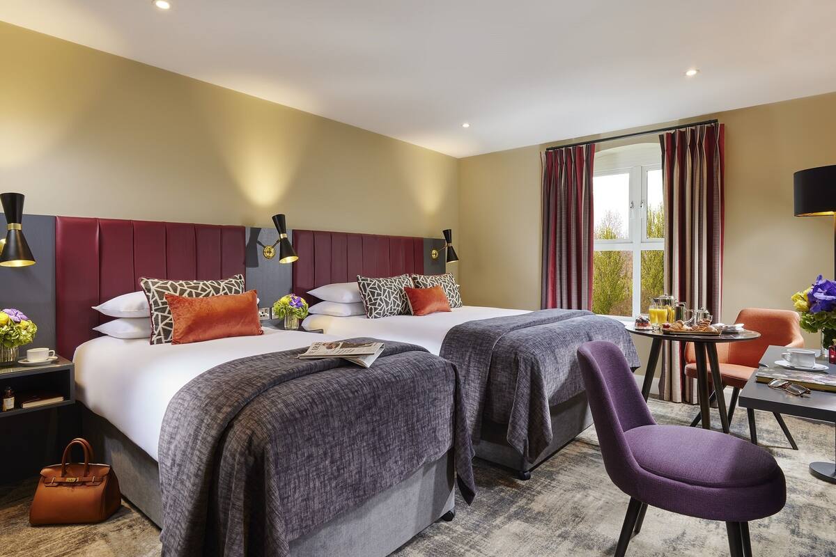 A hotel room with two beds, a dining area, and a view of the outdoors.