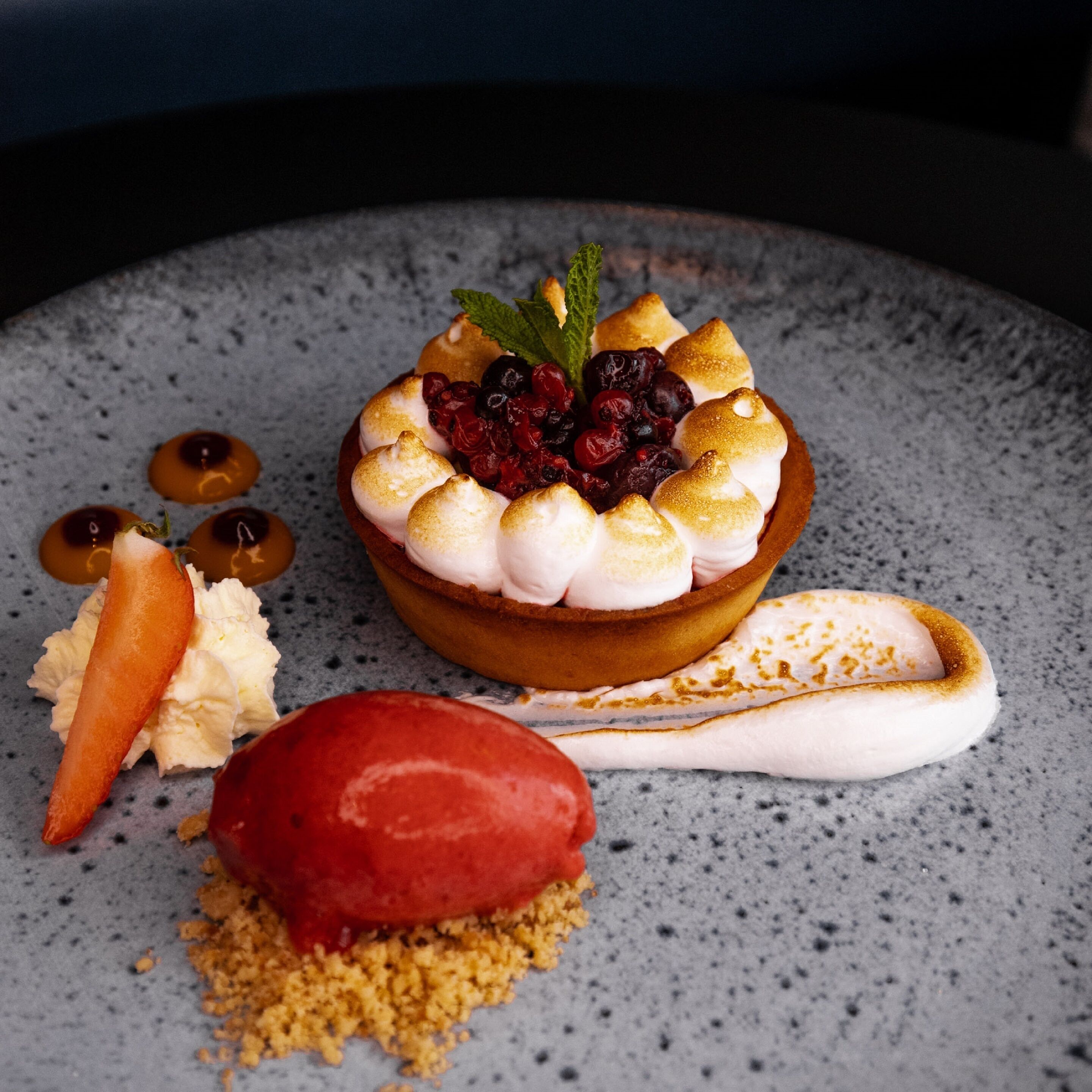 Une assiette de dessert avec une tartelette, des baies et une boule de glace.