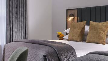 A neatly made bed with a quilted cover, a bedside table with a vase of flowers, and a wall-mounted light fixture.